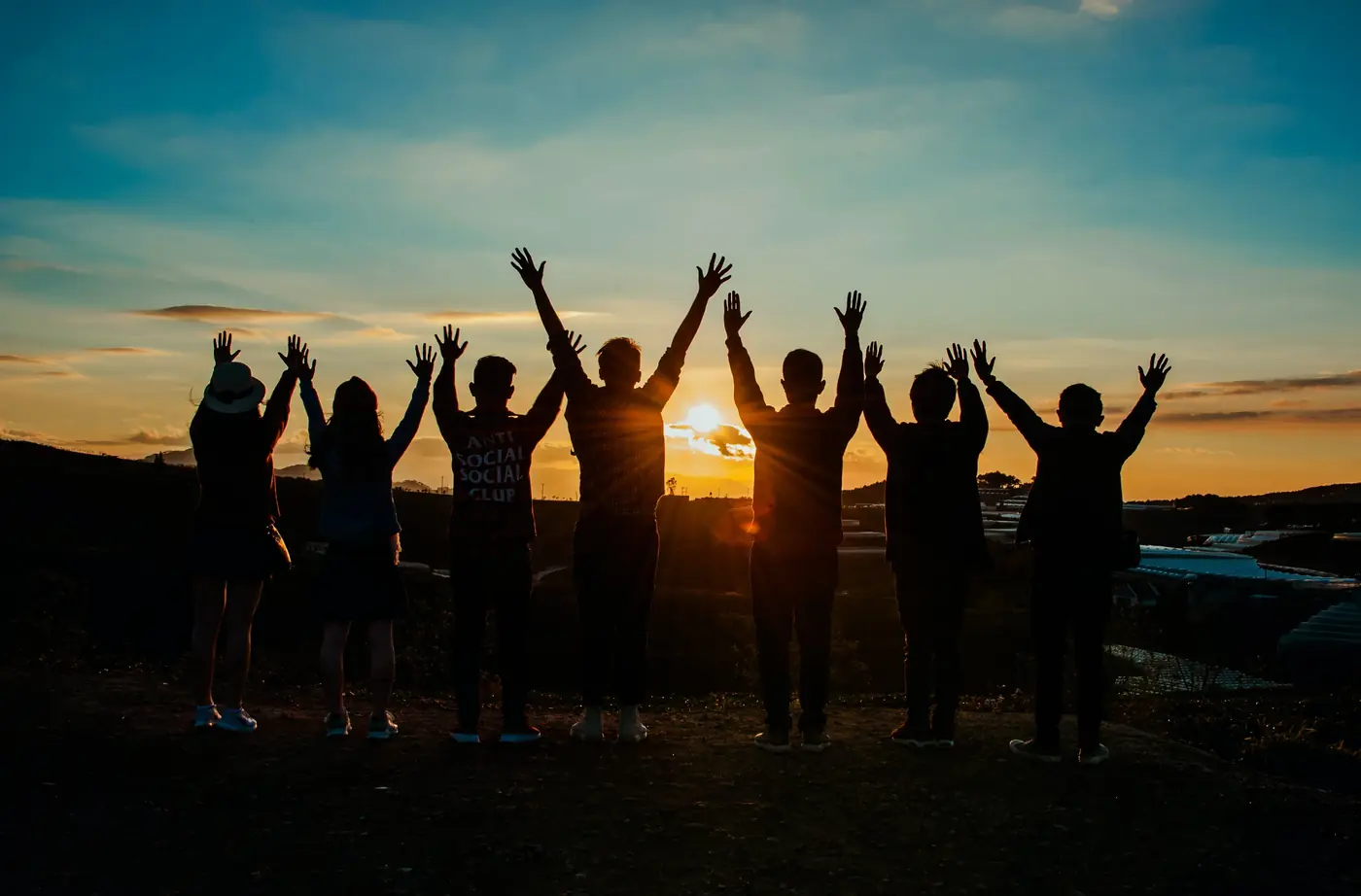 Silhouettes of people raising their arms at sunset
